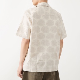 Model wearing Les Deux Dahlia Jacquard Shirt in light sand, rear view showing floral medallion pattern, short sleeves and straight hem