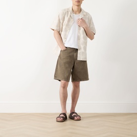 Model wearing Les Deux Dahlia Jacquard Shirt in light sand with camp collar, styled with khaki shorts and brown sandals.
