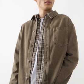 Model wearing Les Deux Chest Pocket Denim Overshirt in light brown denim wash, layered over a plaid shirt and white tee.