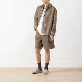 Model wearing Les Deux Chest Pocket Denim Overshirt in light brown denim wash, styled with matching shorts, checked shirt and grey shoes.