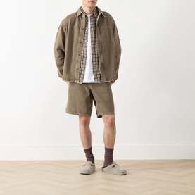 Model wearing Les Deux Washed Denim Shorts in light brown denim wash, styled with a checked shirt, overshirt and grey sandals.
