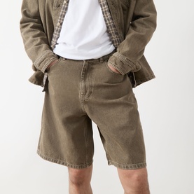 Model wearing Les Deux Washed Denim Shorts in light brown denim wash, styled with a white tee and checked overshirt