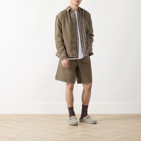 Model wearing Les Deux Washed Denim Shorts in light brown denim wash, styled with a khaki overshirt, check shirt and grey canvas shoes.