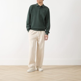 Model wearing Les Deux Script Logo Polo Sweater in pine green with flat collar, styled with cream wide-leg trousers and white trainers.