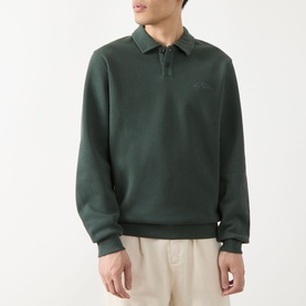 Model wearing Les Deux Script Logo Polo Sweater in pine green with flat collar, zip fastening, and ribbed trims, styled with cream trousers
