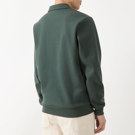 Model wearing Les Deux Script Logo Polo Sweater in pine green, back view, showing flat collar, long sleeves and ribbed trims, styled with cream