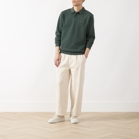 Model wearing Les Deux Script Logo Polo Sweater in pine green with cream wide-leg trousers and white trainers.