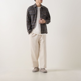 Model wearing Les Deux Light Ivory T-shirt, styled with grey plaid overshirt, cream trousers and grey slip-on shoes.
