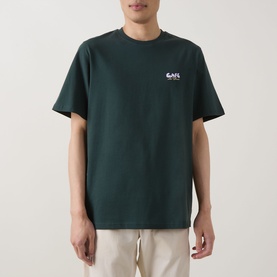 Model wearing Les Deux pine green cotton T-shirt with small chest logo graphic, styled with beige trousers.