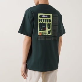 Model wearing Les Deux pine green cotton T-shirt, back view showing illustrated caf&eacute; graphic print in lime green and yellow tones.