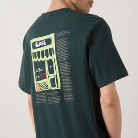 Model wearing Les Deux pine green cotton T-shirt, back view showing yellow caf&eacute; graphic print with text detail