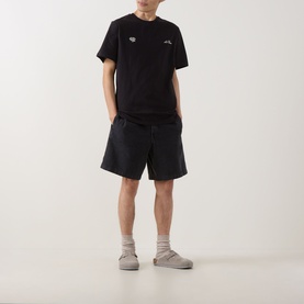 Model wearing Les Deux black cotton T-shirt styled with matching black shorts and grey slip-on shoes.
