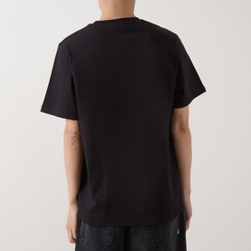 Model wearing Les Deux black cotton T-shirt, rear view, with dark jeans visible at waist.