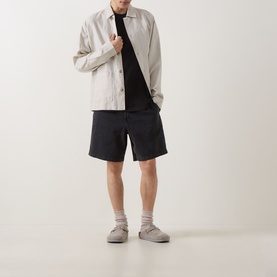 Model wearing Les Deux black cotton T-shirt, styled with a light grey overshirt and dark shorts.