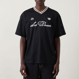 Model wearing Les Deux Logo Mesh Jersey T-Shirt in black with V-neckline, ribbed stripe trim, dropped shoulders and cursive logo branding.