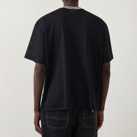 Model wearing Les Deux Logo Mesh Jersey T-Shirt in Tap Shoe Black, rear view showing dropped shoulders and straight hem, styled with dark jeans.