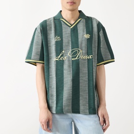 Model wearing Les Deux Stripe Football T-Shirt in pine green with gold stripe jacquard and script logo, styled with light blue jeans