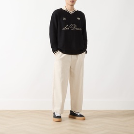 Model wearing Les Deux Waffle Football Top in black with stripe trims and logo detail, styled with cream trousers and navy trainers.