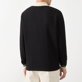 Model wearing Les Deux Waffle Football Top in black, rear view, showing ribbed texture, stripe cuff trims, and open neckline with contrast collar.