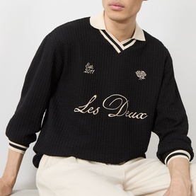 Model wearing Les Deux Waffle Football Top in black with cream V-neck collar, stripe trims, and embroidered script logo detail.
