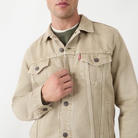 Model wearing Levis The Trucker Denim Jacket in Yellow Sand, showing chest pockets, button fastening and red logo tab, styled with olive crew-neck