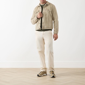 Model wearing Levis The Trucker Denim Jacket in yellow sand, styled with cream trousers and grey trainers