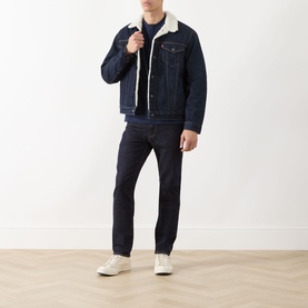 Model wearing Levi's Type III Sherpa Trucker Jacket in dark rinse denim with cream sherpa lining, styled with matching dark jeans and white trainers.