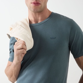 Model wearing Levis Original Logo T-Shirt in dark slate, crew neck, short sleeves, holding a cream cap over shoulder.