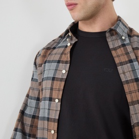 Model wearing Levis Crew Neck T in Mineral Black, styled under an open brown plaid shirt, with subtle chest logo detail visible.