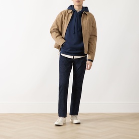 Model wearing Levis Navy Blazer French Terry hoodie, styled with a tan jacket, white tee, navy trousers, and white trainers.