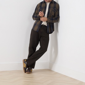 Model wearing Levi's 568 Loose Straight Leg Jeans in Mudslides OD dark wash, styled with plaid shirt and retro trainers.