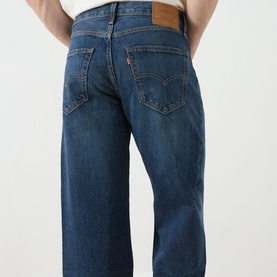Model wearing Levi's 3049 Loose Jeans in Hard Rain mid-blue wash, 100% cotton, shown from behind highlighting back pockets and logo patch.