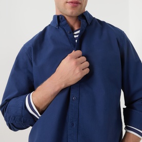 Model wearing Levi's Medieval Blue Garment Dye Reg Shirt in cotton, styled with a white striped top underneath, white stripe cuff detail visible.
