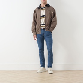 Model wearing Levi's 3049 Slim Jeans in Laugh It Off mid-blue wash, styled with a brown harrington jacket and striped top.