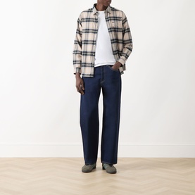 Model wearing Levi's 3049 straight jeans in Keep It Forever Rinse dark indigo wash, styled with a cream plaid overshirt and grey shoes.