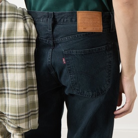 Model wearing Levi's 3049 Straight Jeans in City Boy Blues, dark indigo wash, with a plaid shirt tied at the waist. Rear view.