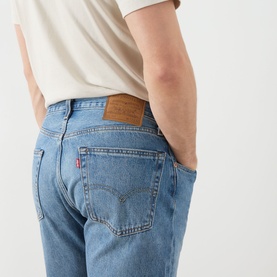 Model wearing Levi's 555 Relaxed Straight Leg Jeans in Indigo Champion, showing rear five-pocket detail, logo patch, and red tab. Styled with white