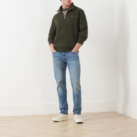 Model wearing Levi's Original Housemark Logo Half-Zip Sweater in dark green with raised collar, styled with light blue jeans and white trainers.