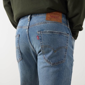 Model wearing Levi's 502 Tapered Leg Jeans in Its Been A While Selvedge, mid-rise with faded wash, rear logo patch visible, styled with olive