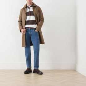 Model wearing Levis 3049 Tapered Jeans in Stonewash Stretch, styled with a tan trench coat, striped polo and dark loafers