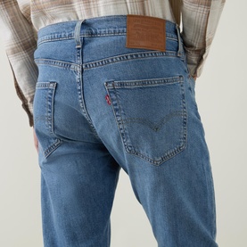 Model wearing Levi's 502&trade; Tapered Leg Jeans in Just Say Hi mid-wash blue, showing rear logo badge and tobacco stitching, styled with plaid shirt.