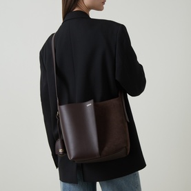 Model carrying Loewe Bilbao Medium Bucket Bag in Dark Chestnut, suede and leather with gold-tone hardware, worn cross-body over black blazer.