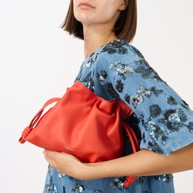 Model carrying Loewe Flamenco Mini Clutch in Sunrise Orange, soft calfskin with drawstring knot detail, styled with a floral blue dress.