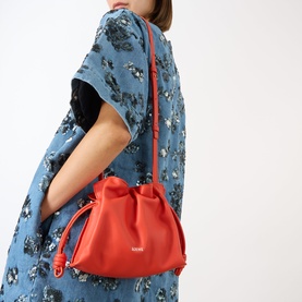 Model carrying Loewe Flamenco Mini Clutch in Sunrise Orange with silver-tone logo, drawstring knot detail, worn crossbody over floral blue dress.