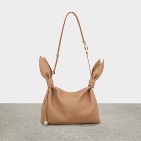 Camel leather shoulder bag with knotted bow strap details, gold-tone charm, and single adjustable strap