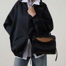 Model carrying Loewe Amazona 180 Medium Top Handle Bag in black smooth leather with silver-tone hardware, worn crossbody, styled with black jacket