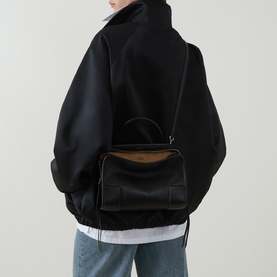 Model carrying Loewe Amazona 180 Medium Top Handle Bag in black smooth leather, silver-tone hardware, worn over shoulder with black jacket