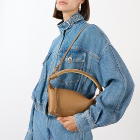 Model carrying Loewe Cala Top Handle Pouch Bag in mocha, smooth lambskin with silver-tone hardware and crossbody strap, styled with denim jacket
