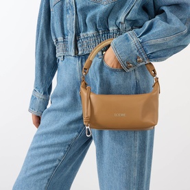 Model carrying Loewe Cala Top Handle Pouch Bag in mocha lambskin, silver-tone hardware, handwoven handle, styled with denim jacket and jeans