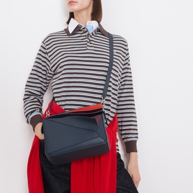 Model carrying Loewe Puzzle Edge Small Crossbody Bag in Multicolour Deep Navy with gold-tone hardware, worn crossbody with striped top and red skirt.